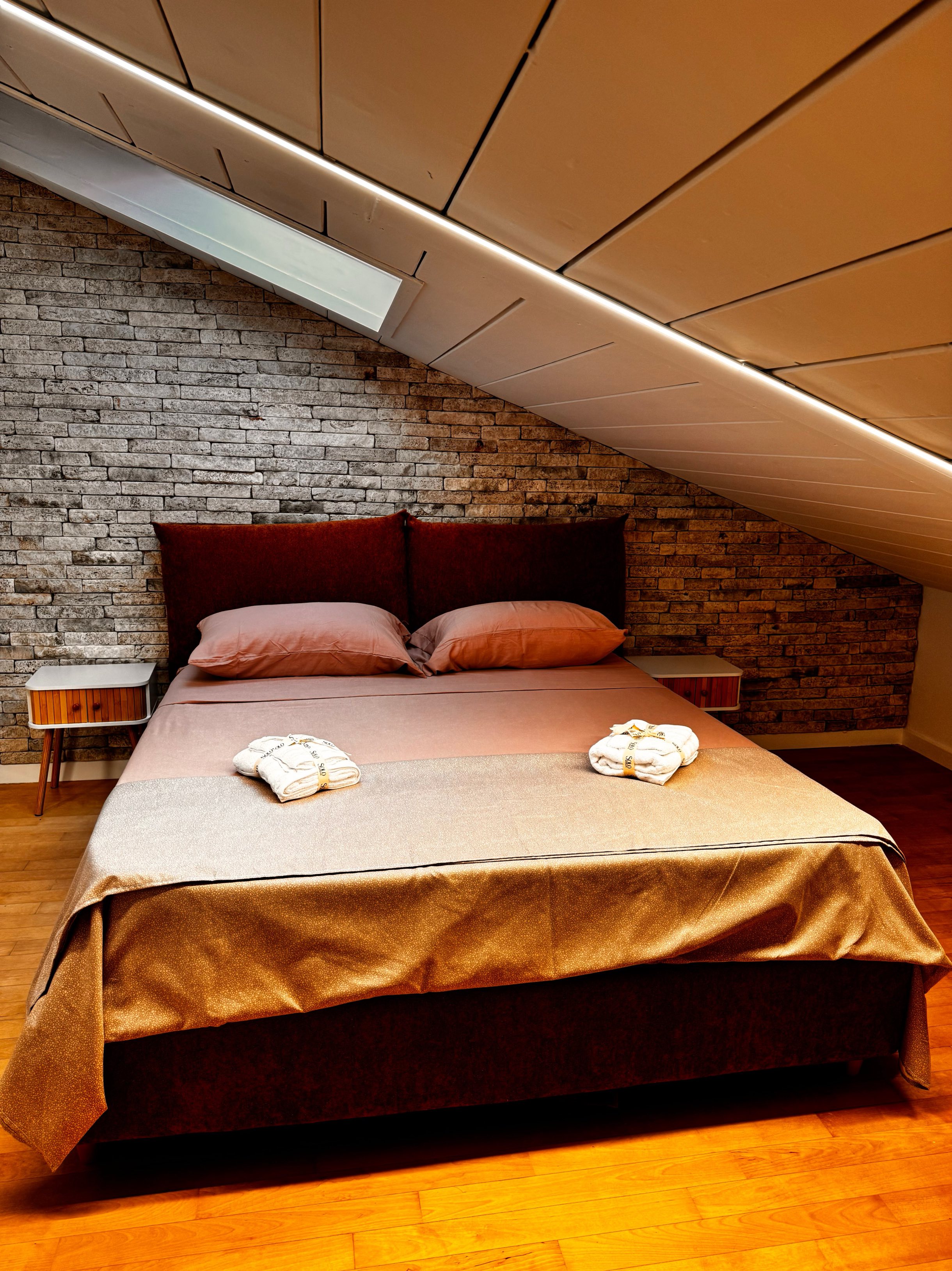 Camera da letto dell'attico con testata in pietra e biancheria calda